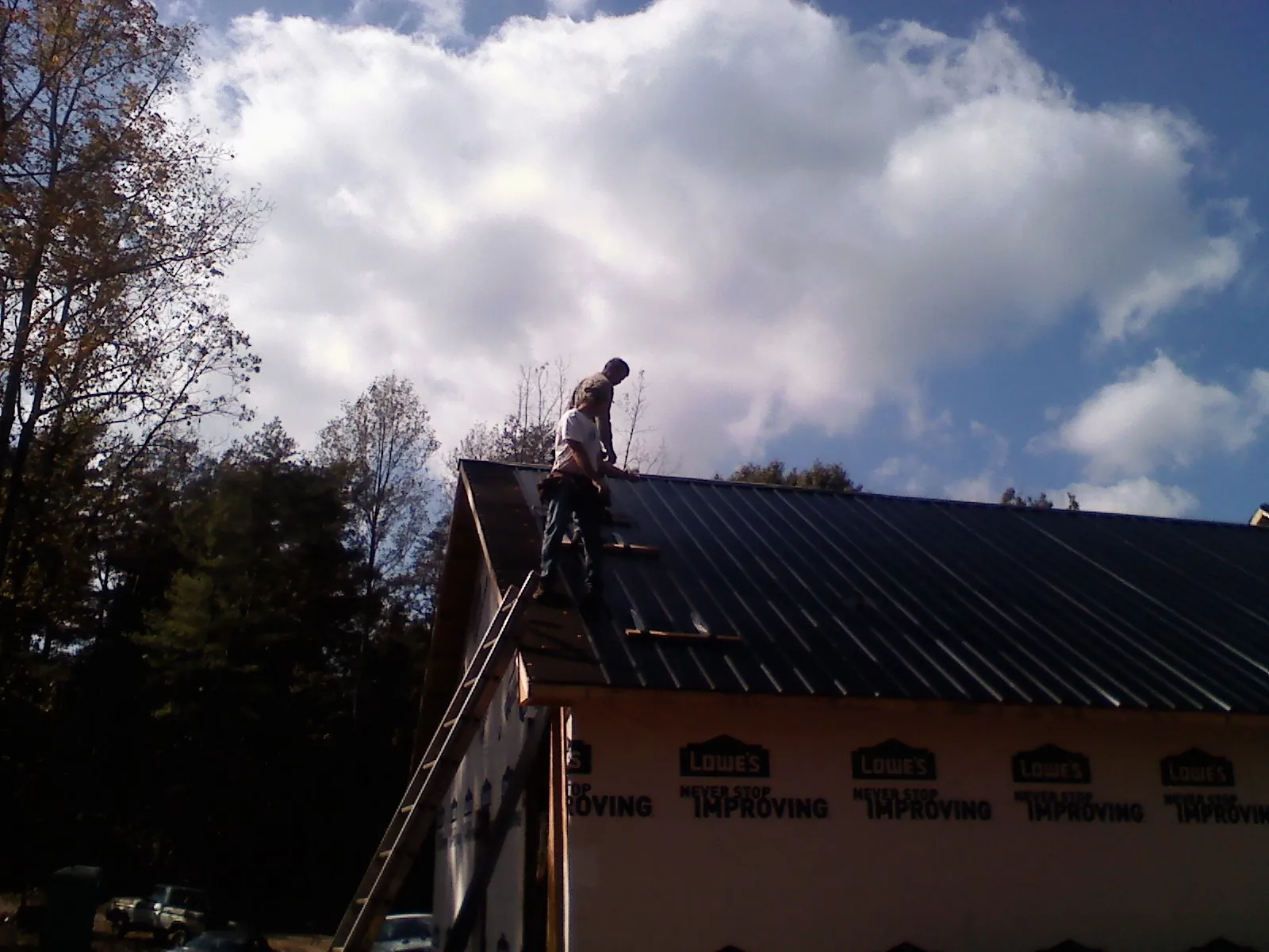 Roofer fastening dark metal panels high against a cloudy sky, from a Roof Inspection job in Freedom