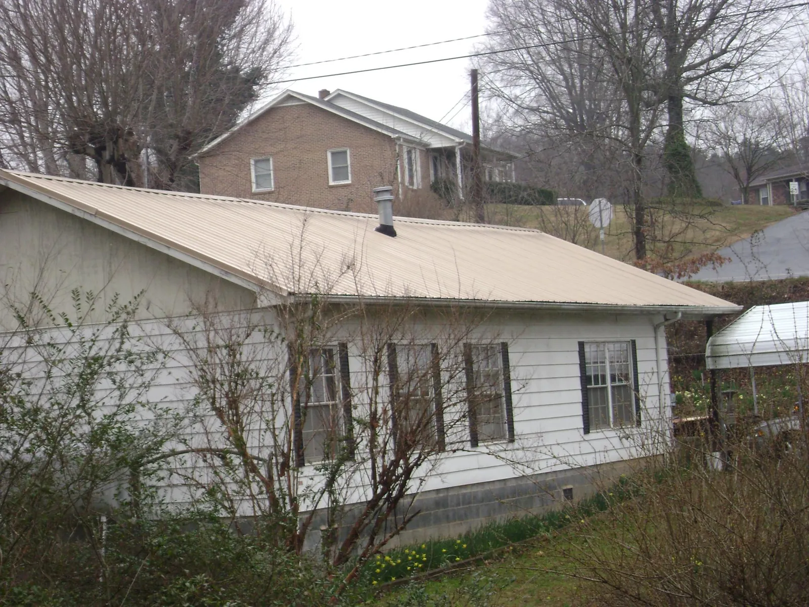 Tan metal roof on a white sided house set into a hillside — Commercial Roofing by Roofing Brothers in Freedom